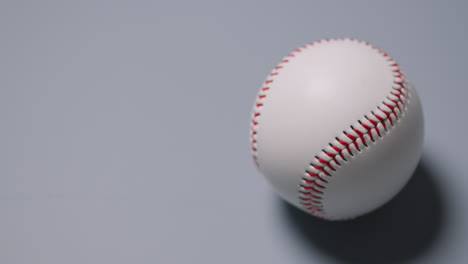 Close-Up-Shot-Of-Hand-Picking-Up-Baseball-Ball-Against-Grey-Background